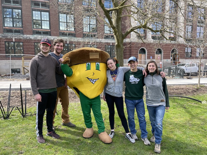 five students standing with Oakie Acorn, giant yellow acorn mascot