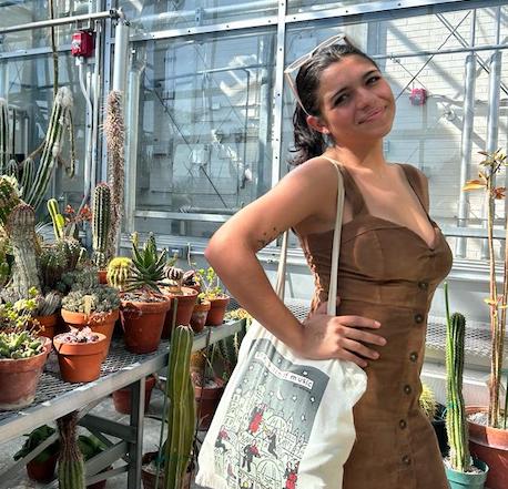 young woman wearing a brown dress standing in greenhouse near potted cactus plants