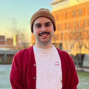 Man standing in front of snow dusted quad with a sunset lighting up the building in the background. 