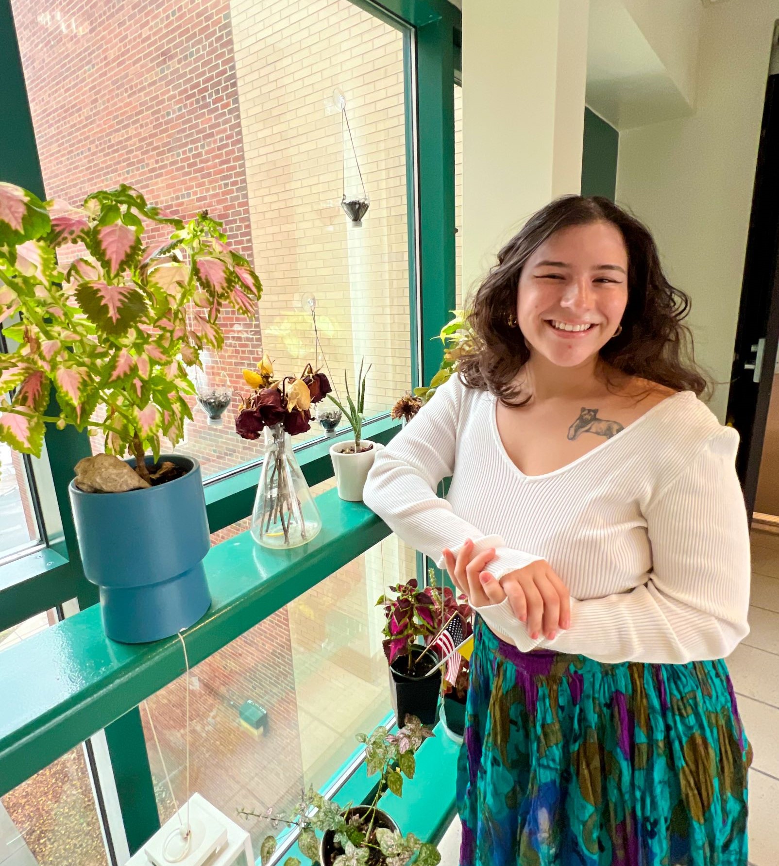 Woman standing next to several plants on a windowsill. 