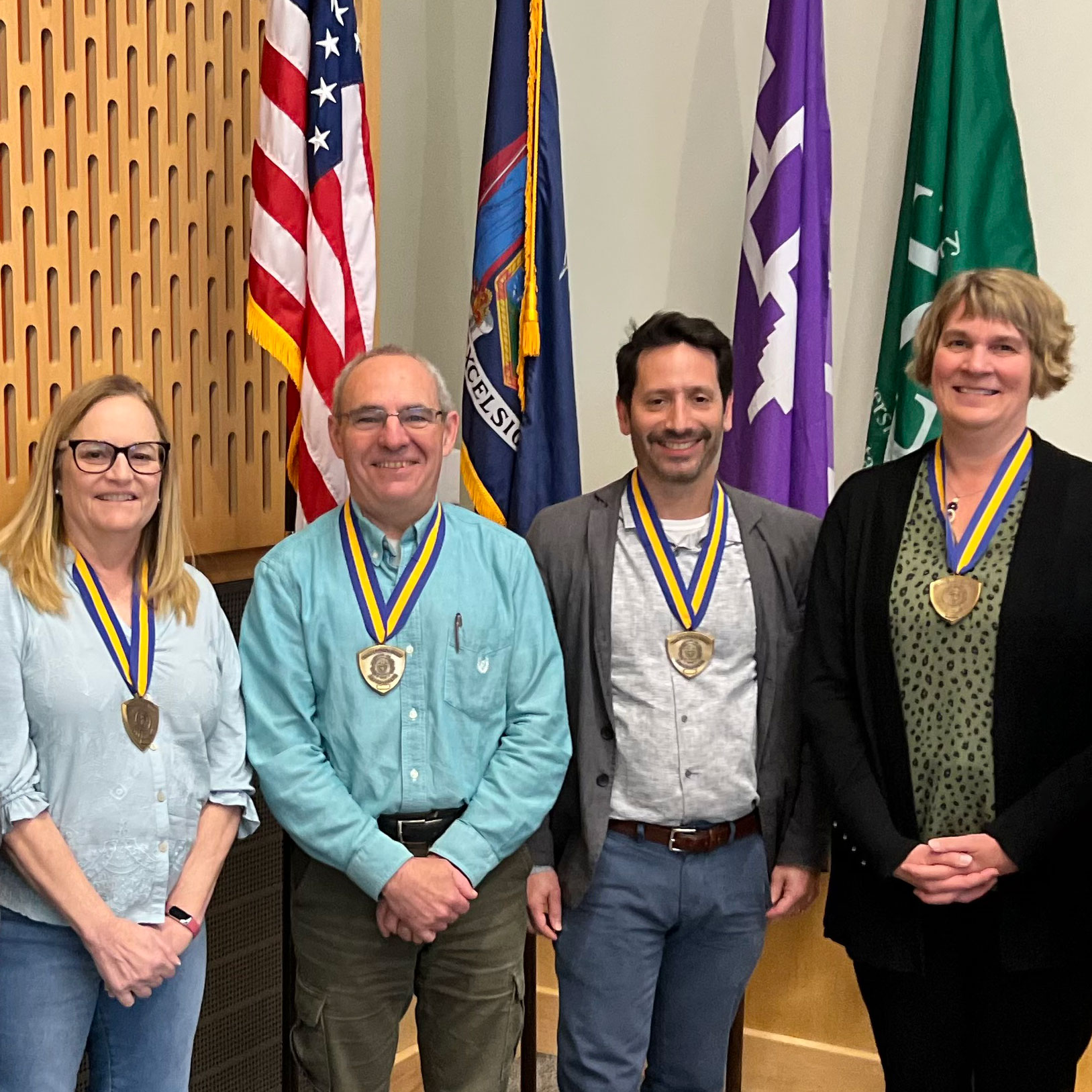 Four people wearing medallions standing in front of flags