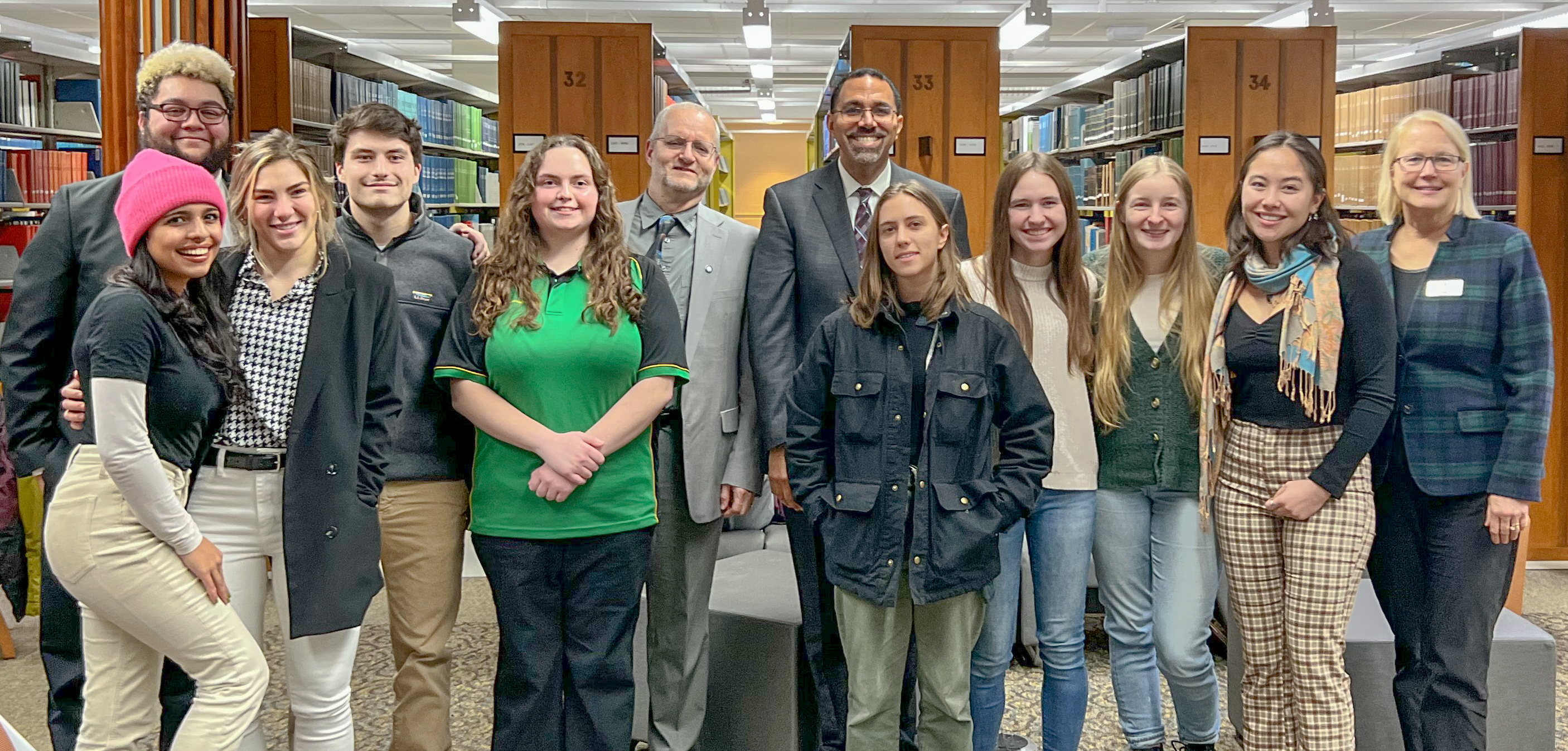 Group of people looking at the camera and standing with books in the background. 