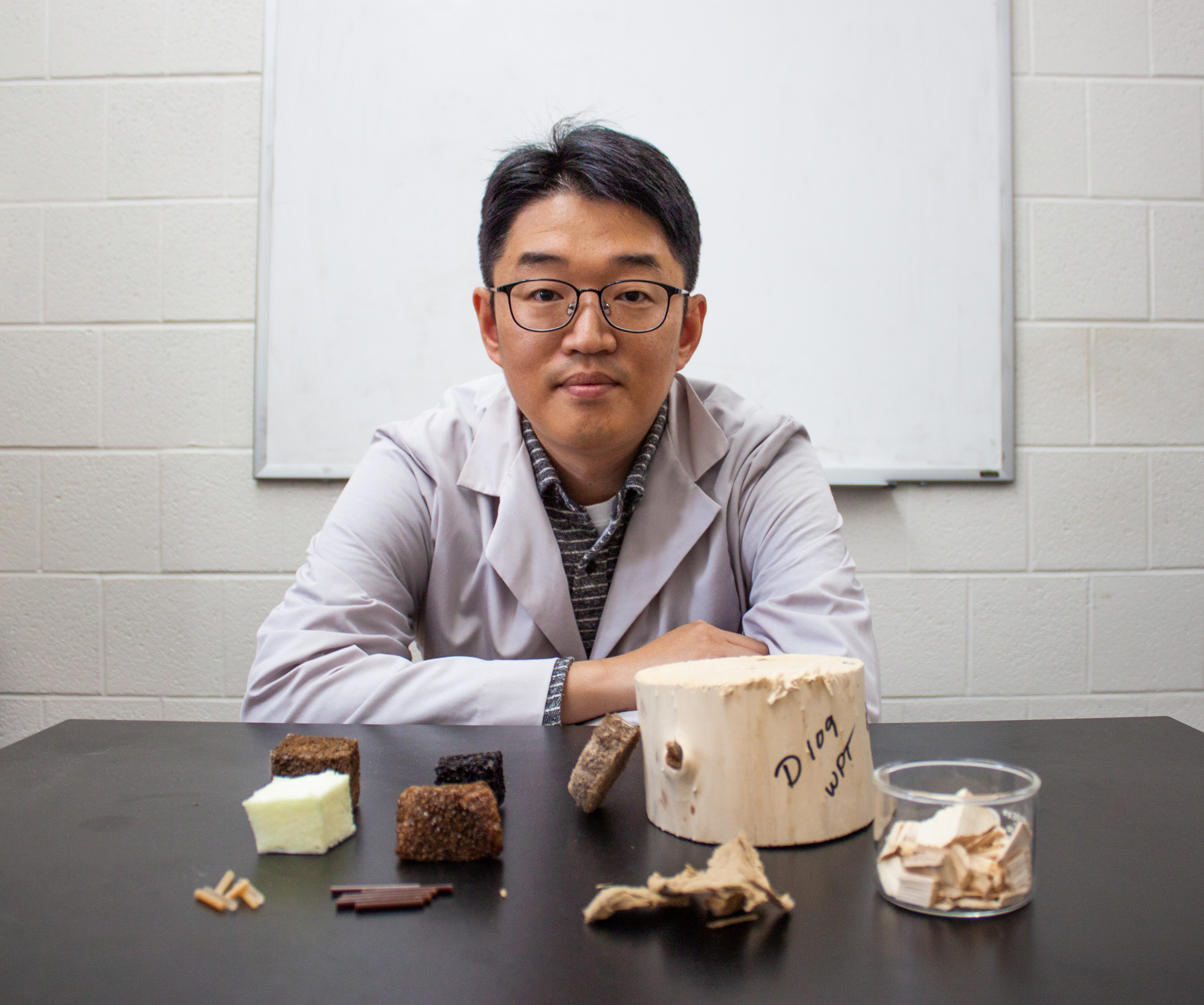 Man with a lab coat sitting with various wooden and foam materials in front of him. 
