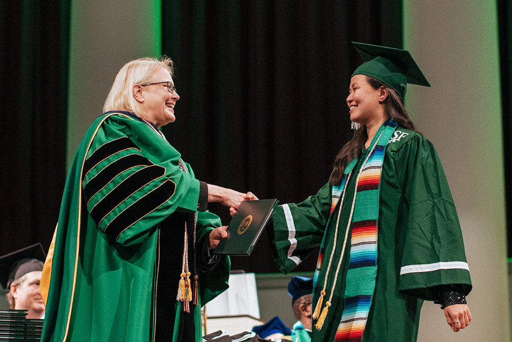 Two women in green graduation gowns shaking hands.