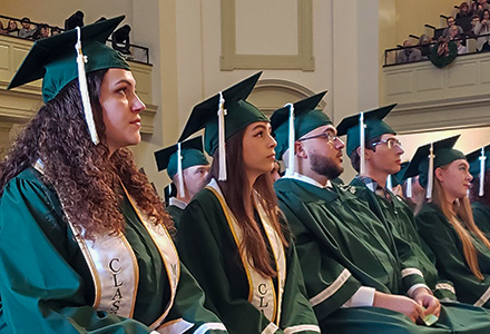 Women and men sitting wearing green graduation regalia.