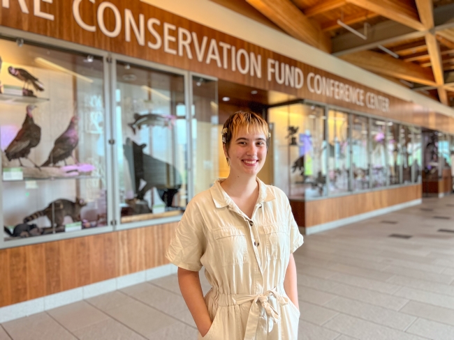 Woman in a white jumper standing in front of a bunch of taxidermied animals behind glass cases. Text at the top says "Conservation Fund Conference Center" 