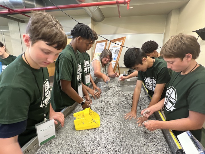 Teenagers in green T-shirts working at a hydrology table.