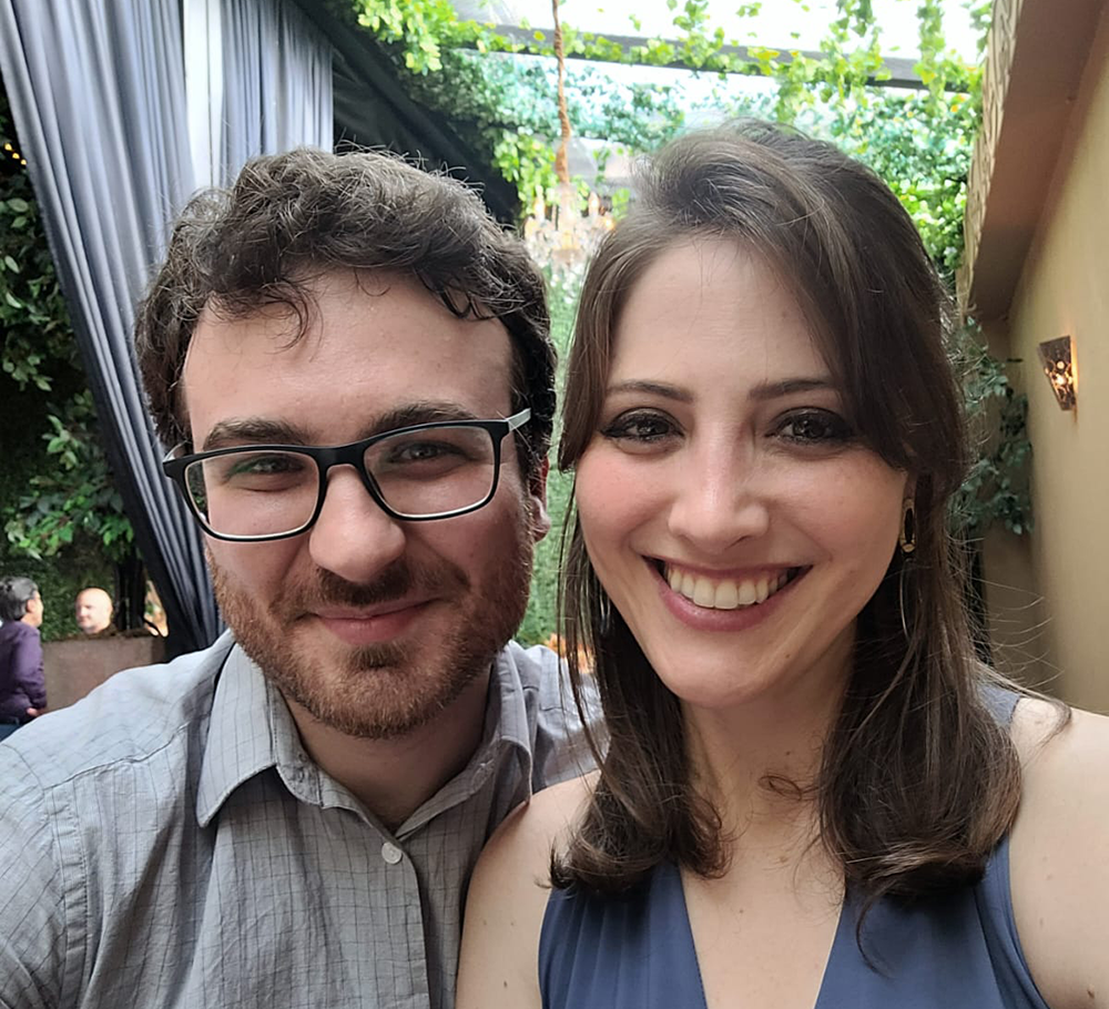 Man in a blue shirt next to a woman in a purple dress. They are close to the camera in a selfie style format 