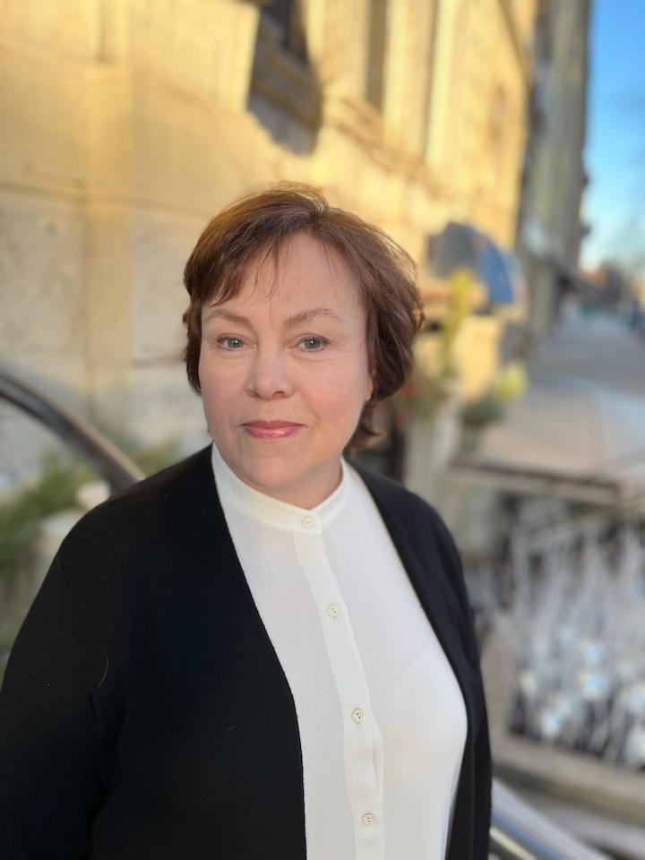 Woman in dark sweater and white shirt standing outside