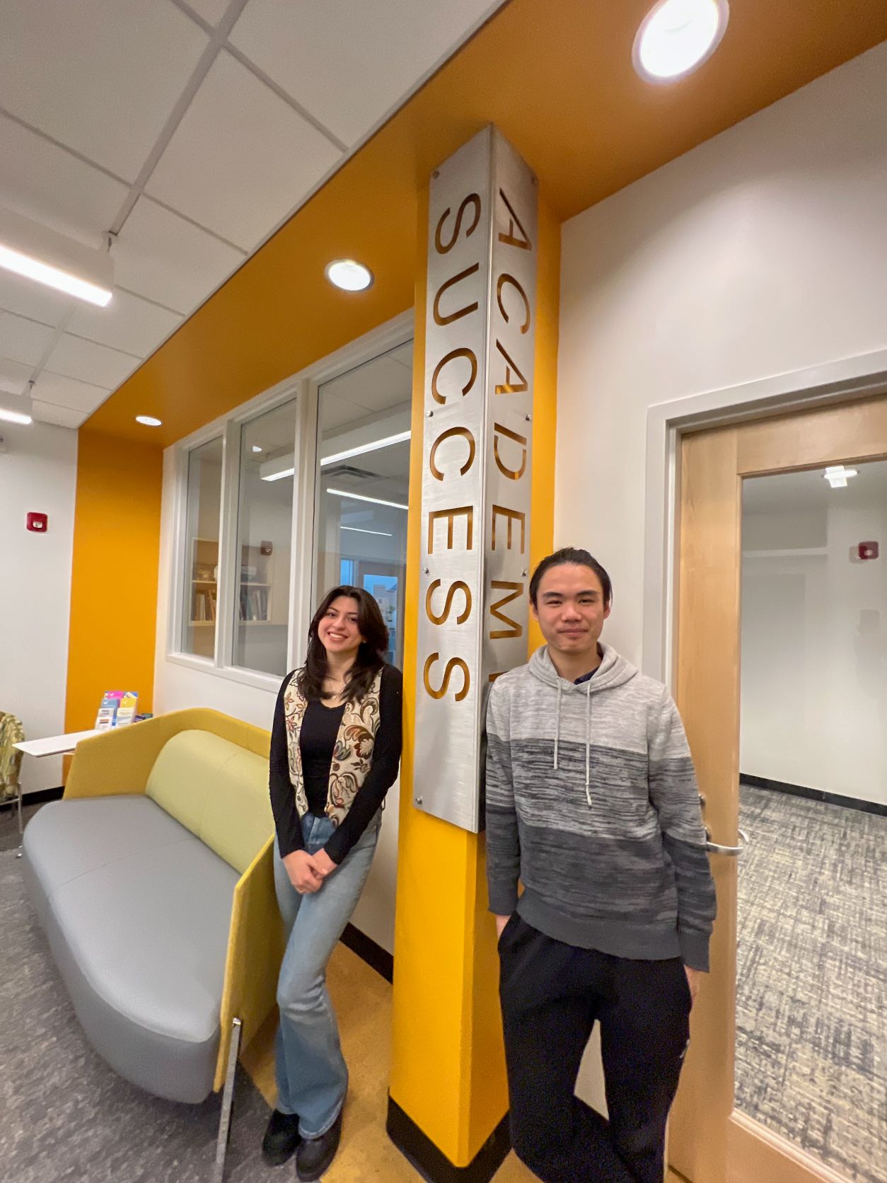 Woman and man standing back to back against a yellow pillar that says Academic on the right, and success on the left. 