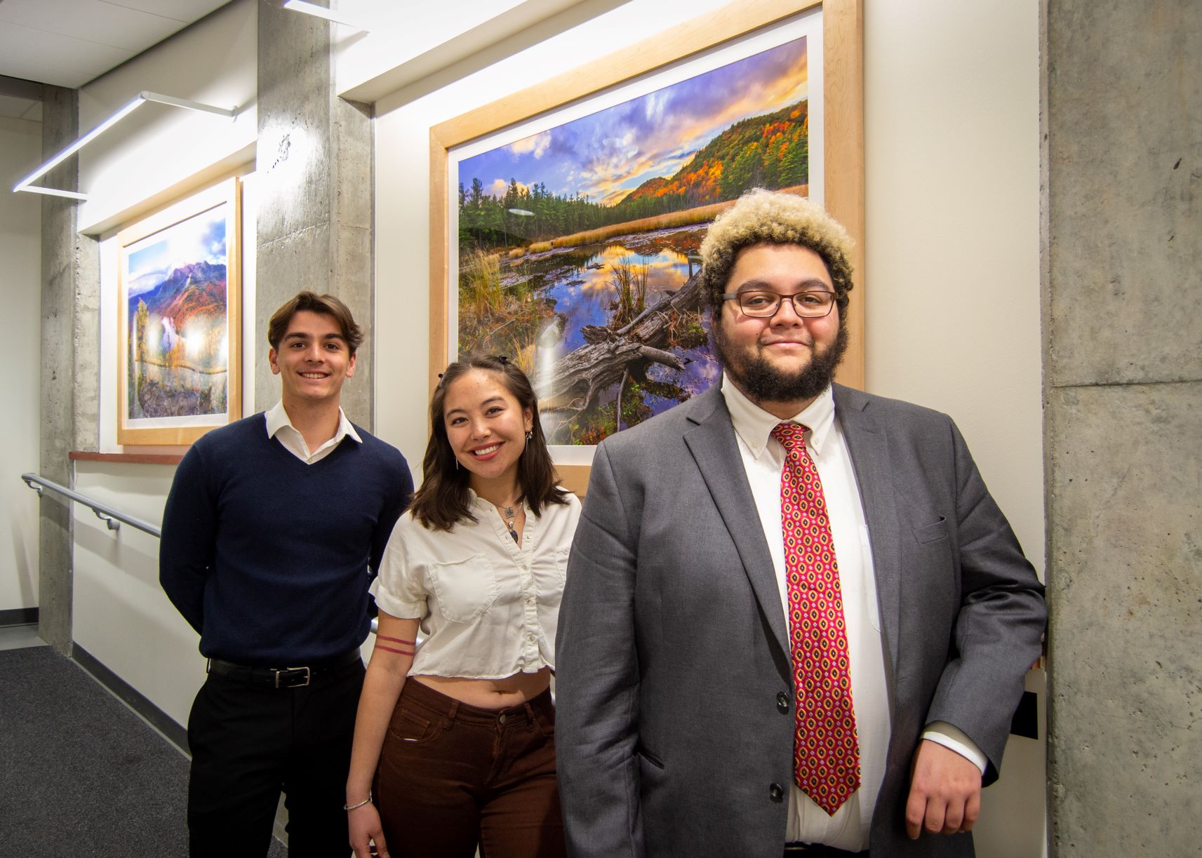 Two men and a woman in professional dress, standing against a railing with pictures of nature in the background.