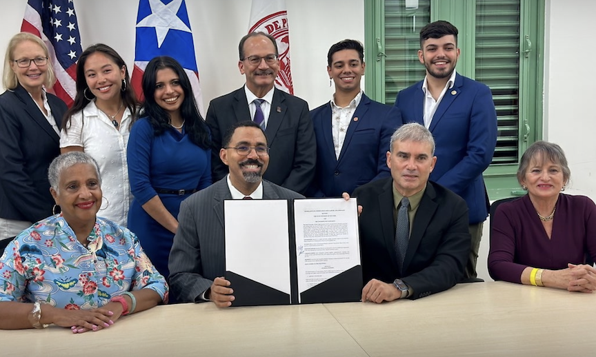 Ten people posing with a signed document. Six are standing, four are sitting.