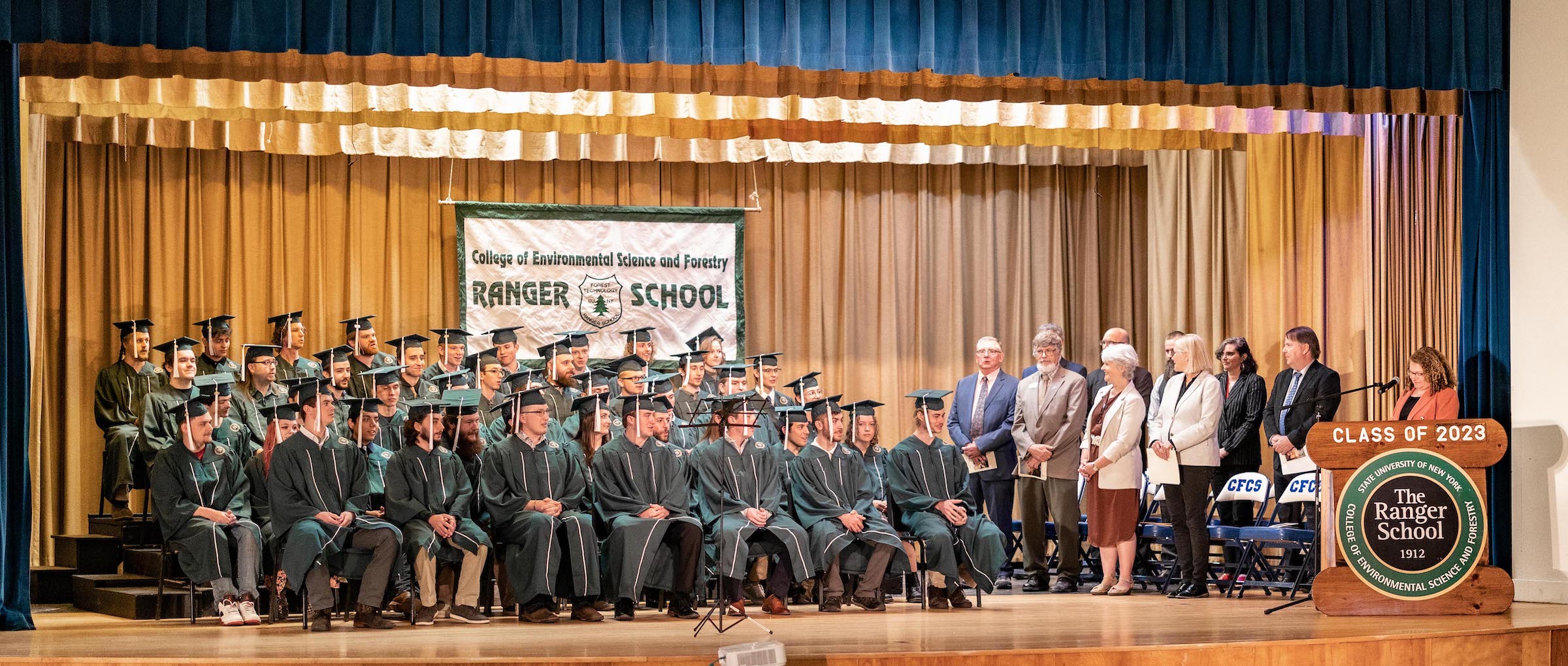 Graduates in green gown on stage with teachers