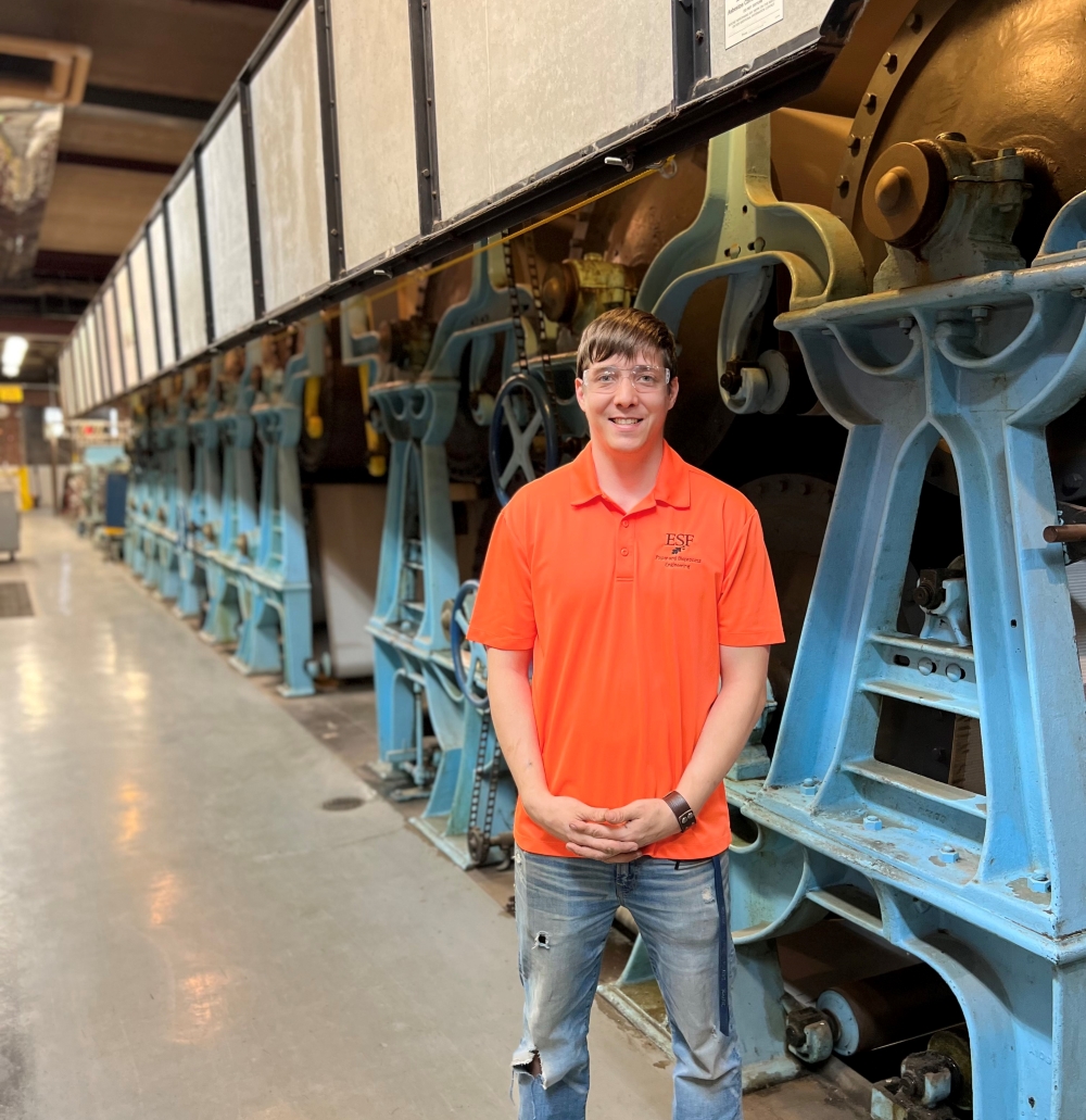 Man standing in front of a large industrial machine with the color blue. 