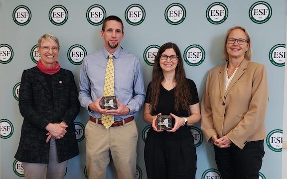 Four people standing in front of an ESF backdrop. Man and woman in middle are holding awards.