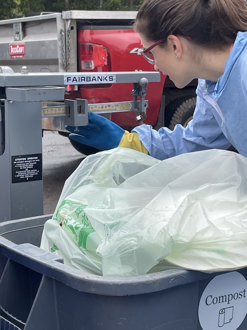 Woman wearing blue PPE weighs a bag of compost.