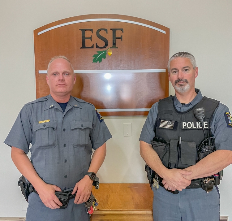 Two men in police uniform standing near a wooden sign. 