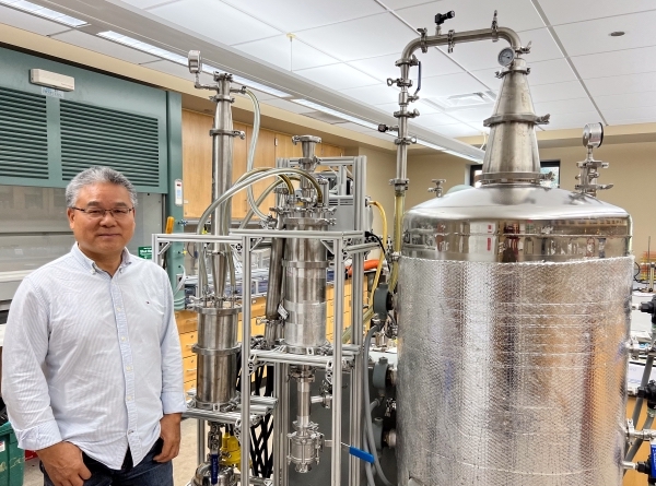 Man in white button-down shirt stands next to vacuum stripping and absorption prototype.