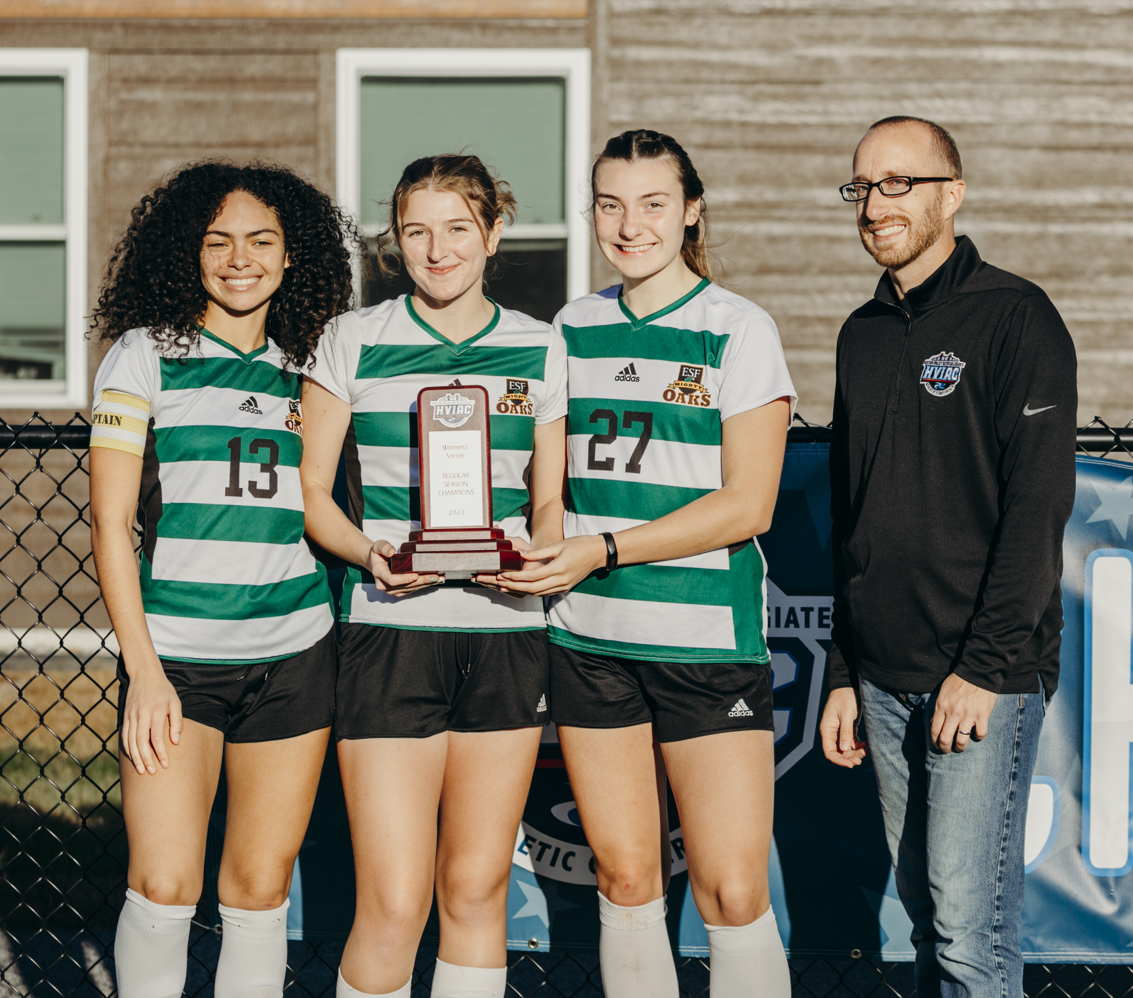 Three women in green and white striped shirts and Amanda in a blue shirt pose with a trophy.