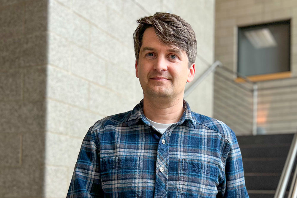 Man with salt and pepper hair wearing a blue plaid flannel shirt standing in a stairwell.