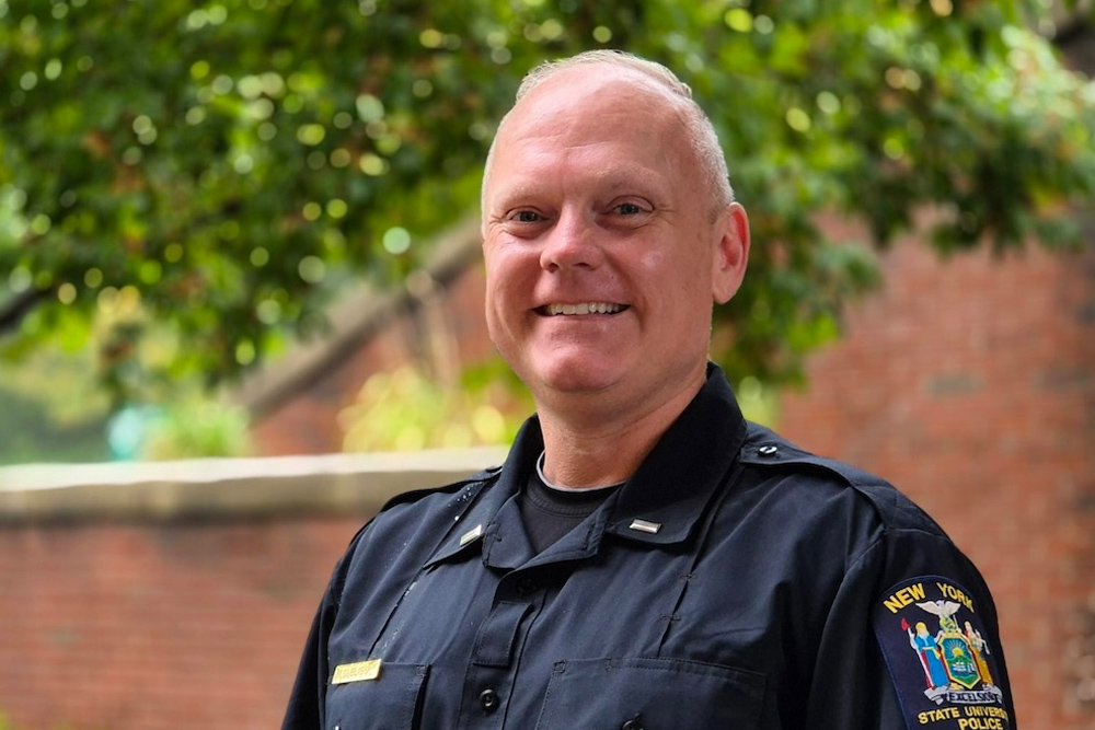 Police officer in blue uniform standing in front of brick wall.