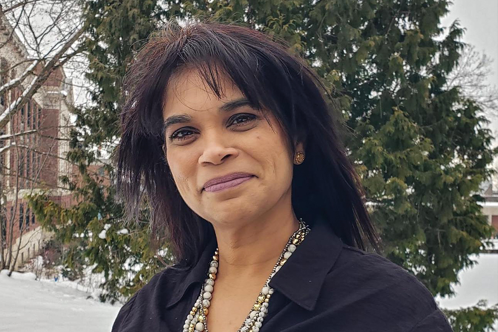 Woman with dark hair wearing a black suit jacket standing outside in front of a tree in the winter.