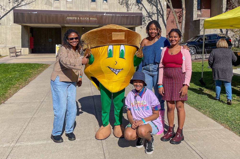 A family of four standing with giant yellow acorn mascot.
