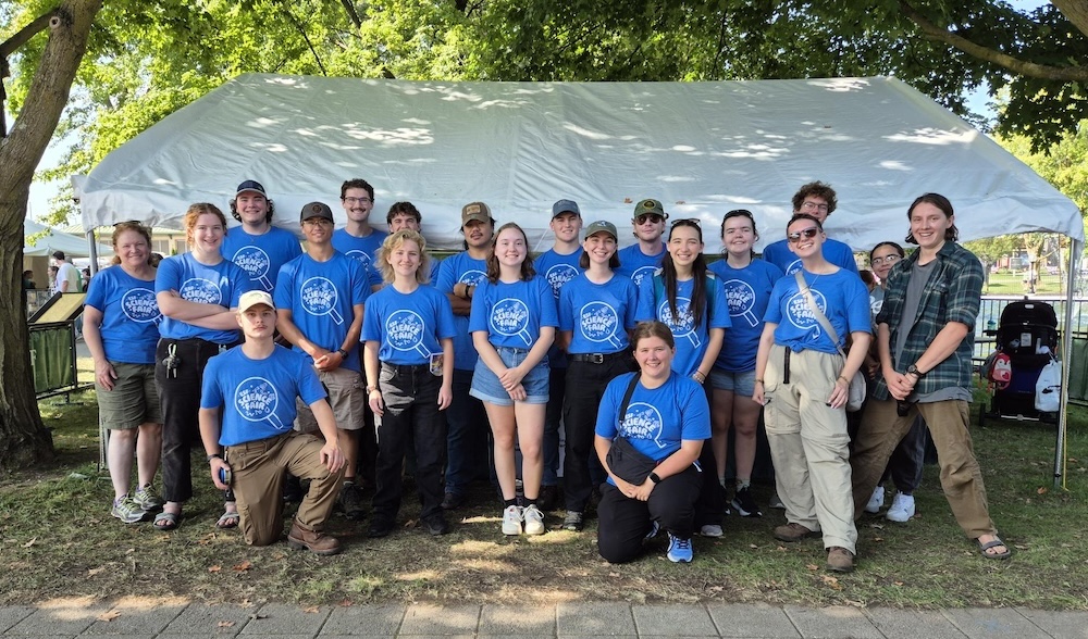 Large group of people wearing blue shirts standing outside in front of a white tent.