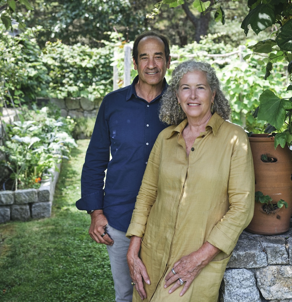 Man in blue shirt standing next to woman in pale yellow dress in a garden.