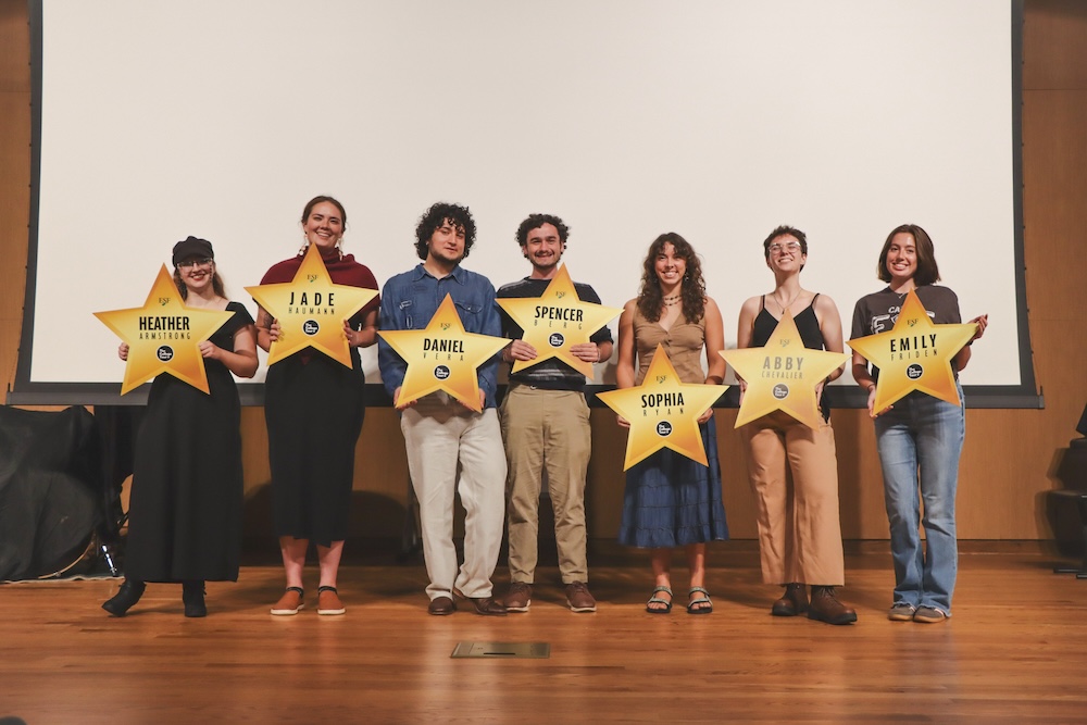 Seven students - men and women - stand holding gold stars bearing their names.