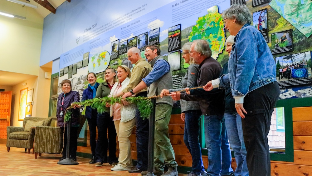 Group of people standing behind a garland for a ribbon cutting.
