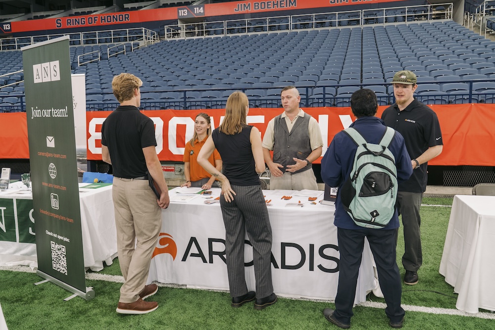 People standing in front of and behind a table with a white tablecloth and an Arcadis logo.