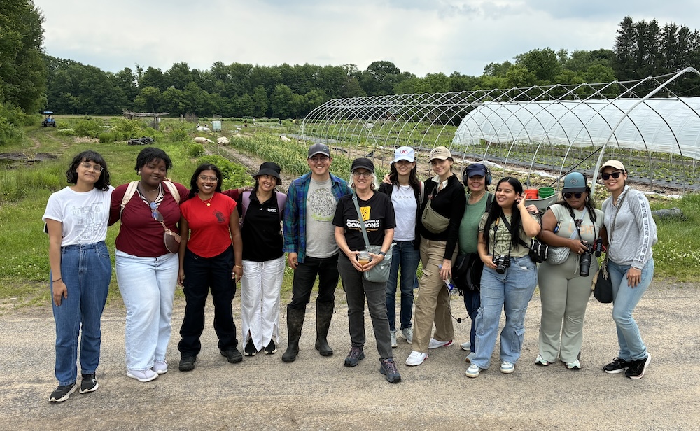 Twelve people standing in front of a field at a farm.