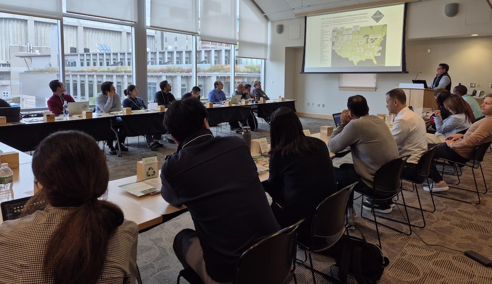 people sitting around tables looking at a screen with map of the United States.