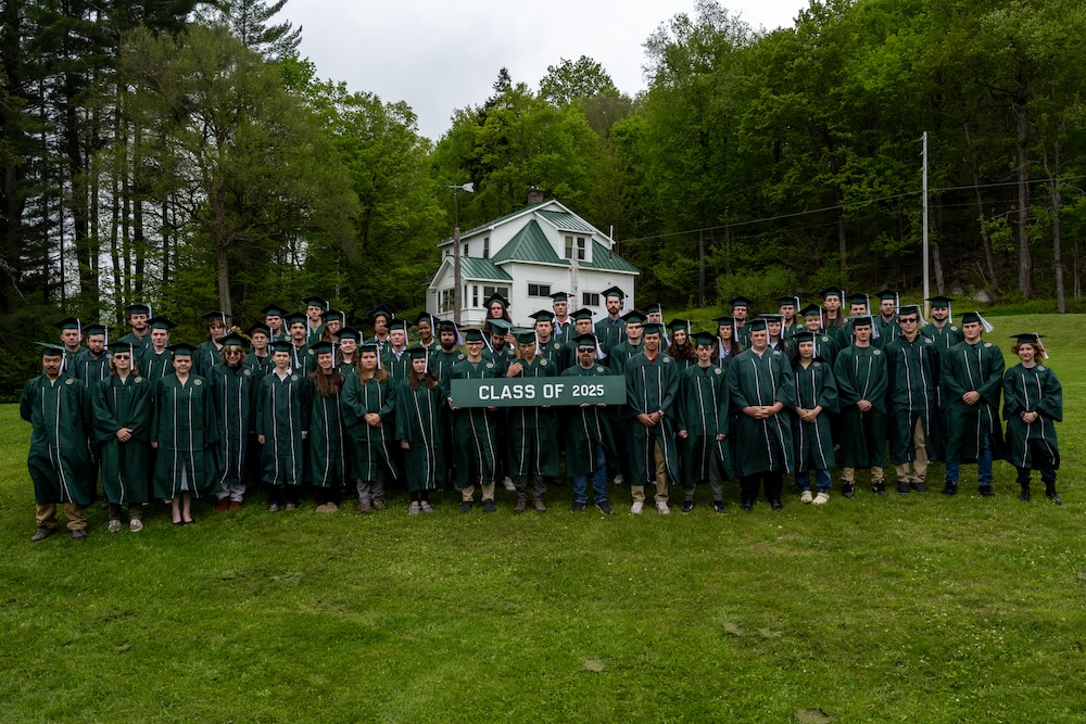 Graduates wearing green caps and gowns standing outside with a class of 2025 sign