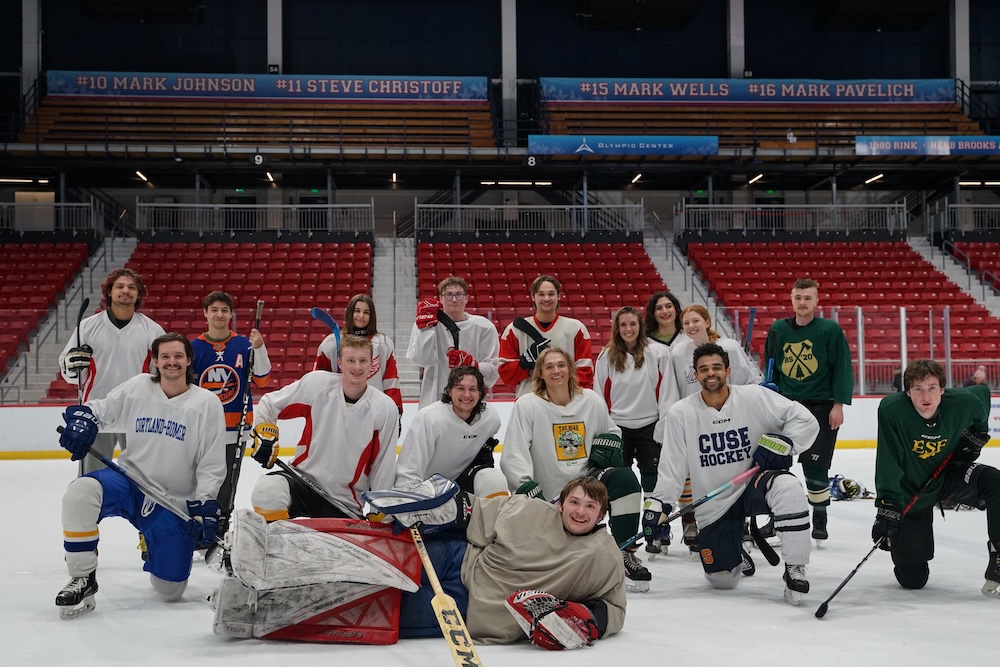 A group of approximately 20 ESF club hockey players pose together on an indoor ice rink, wearing mixed hockey jerseys, helmets, gloves, and skates, with one goalie lying on the ice in front of the group. 