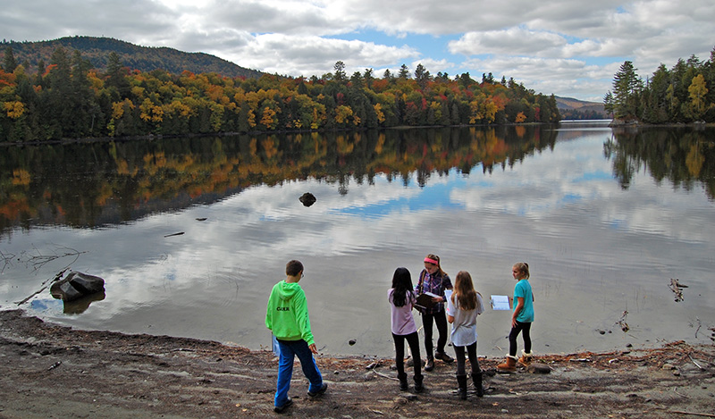 children with notebooks near a lake