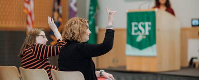 Two people seated with raised hands in an auditorium.