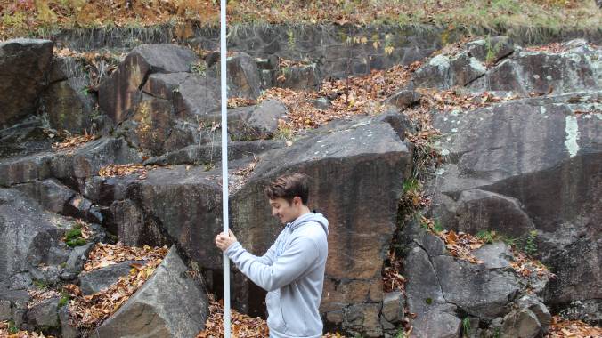 Student surveying in a forest next to boulders