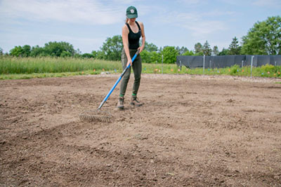 Jess Proctor raking a soil to prepare for meadow planting in Skaneatles