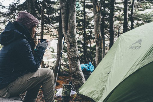 A woman holding a cup sitting next to a tent