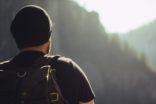 A man wearing black cap and t-shirt with a black backpack facing away from the camera