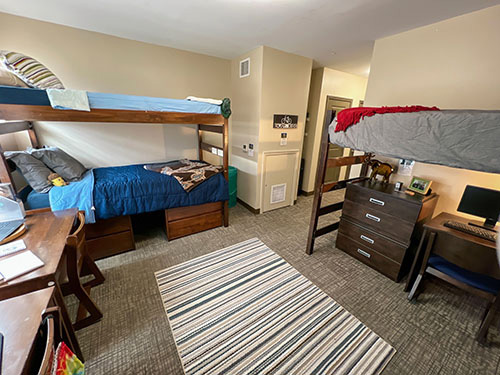 Triples room in Centennial hall. Bunk beds and study table is in the room and a rug is in the middle of the room