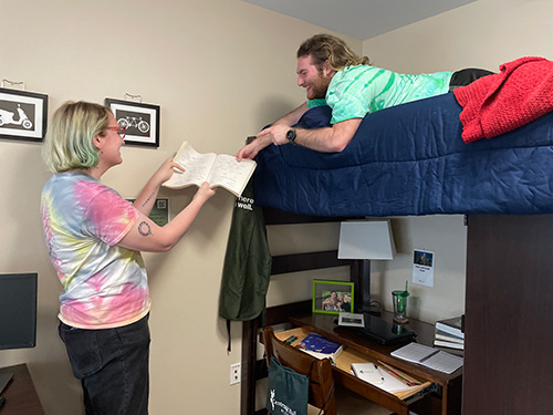 A student on a bunk bed talking to another student who is holding a book