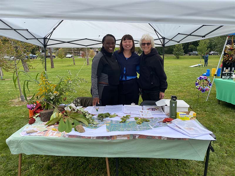 Three women in mile market showing maps of food forests