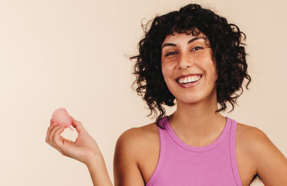 a gril in pink tank top holding a menstrual cup