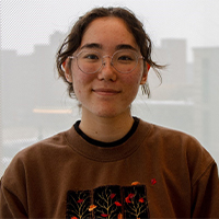 A headshot of Shannon Dunn. She is giving a soft smile. Her hair is brown and pulled back. She is wearing thin-framed glasses and a brown sweater with autumn leaves on it.