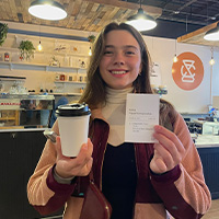 Anna standing with a coffee mug in front of Moon Cafe